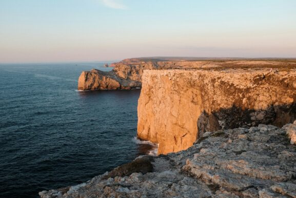 Rocky Algarve cliff overlooking golden Atlantic waters at sunrise in April